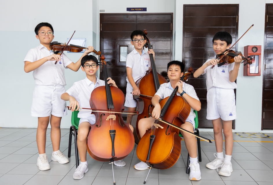 Three children in white shirts playing cellos together in a practice session.